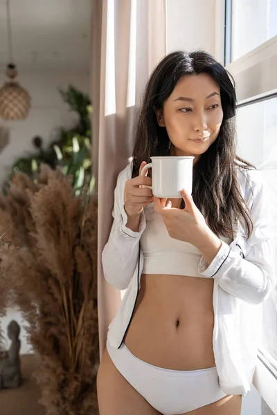 早上喝咖啡是我每天的例行公事 年轻美丽的亚洲女人穿着内裤 早上站在窗边喝咖啡 — 图库照片