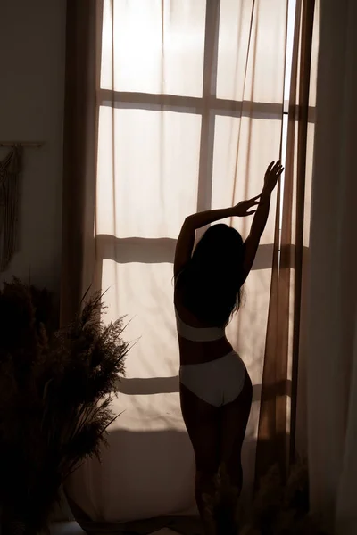 一个性感的女人 身材苗条 身穿内裤 站在窗前 早上醒来后躺在床边 后视镜 — 图库照片
