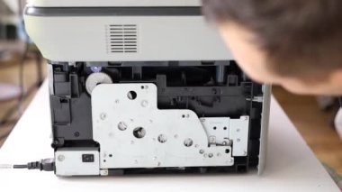 printer repair technician. A male handyman inspects a printer before starting repairs in a client's apartment.