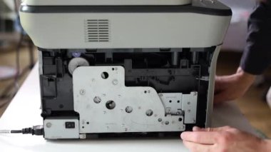 printer repair technician. A male handyman inspects a printer before starting repairs in a client's apartment.