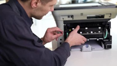printer repair technician. A male handyman inspects a printer before starting repairs in a client's apartment.