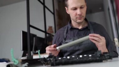 printer repair technician. A male handyman inspects a printer before starting repairs in a client's apartment.