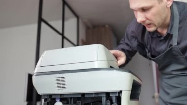 printer repair technician. A male handyman inspects a printer before starting repairs in a client's apartment.
