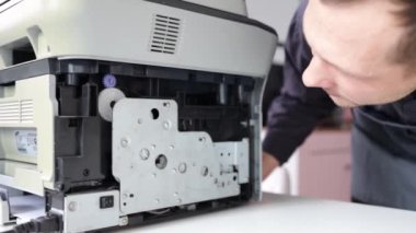 printer repair technician. A male handyman inspects a printer before starting repairs in a client's apartment.