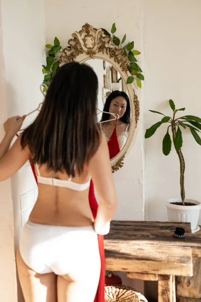 漂亮的年轻亚洲女人站在衣橱 时尚的镜子前 正在检查红色衣服的外观 — 图库照片