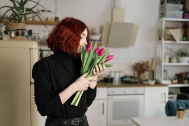Mutlu kadın bir buket lalenin tadını çıkarıyor. Ev hanımı bir demet çiçeğin ve mutfağın tadını çıkarıyor. Eviniz güzelmiş. Alerji yok.