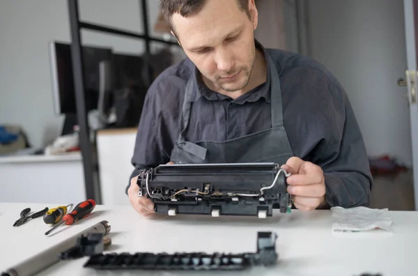 printer repair technician. A male handyman inspects a printer before starting repairs in a client\'s apartment.