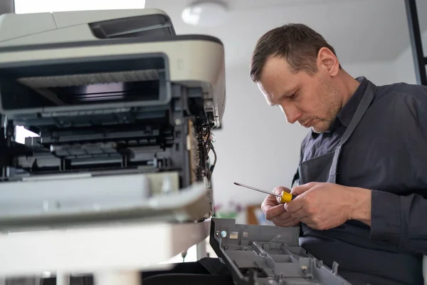 printer repair technician. A male handyman inspects a printer before starting repairs in a client's apartment.