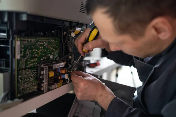 printer repair technician. A male handyman inspects a printer before starting repairs in a client\'s apartment.