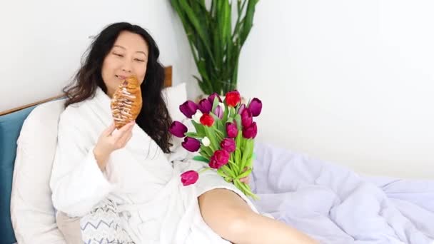 ベッドで幸せなアジアの女性 コーヒーとクロワッサンとの美しい朝 家での完璧な朝 — ストック動画