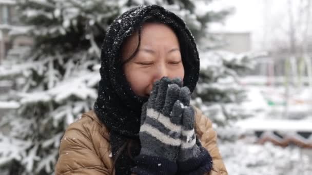 寒い風の中で外を待っている冬の外で凍った若いアジアの女性のクローズアップ顔 手をこすり 手のひらに吹いて暖かく保つために 低温に苦しんで — ストック動画