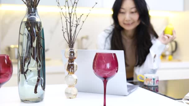 年轻迷人的亚洲女人正坐在厨房的工作台上 在笔记本电脑上工作 在线药方网站 在家里找一份浪漫晚餐的食谱 — 图库视频影像