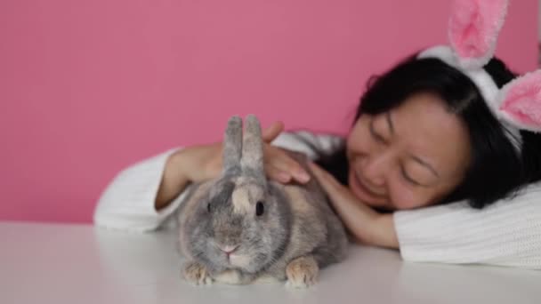 Смішна Щаслива Дівчина Вухами Кролика Тримає Сірого Кролика Рожевому Фоні — стокове відео