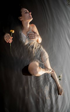 Gün batımında gölde elinde zambak tutan güzel genç bir kadın. Gün batımında romantik, ıslak bir kızın portresi, sıcak güneş, doğal bir kadın güzelliği.