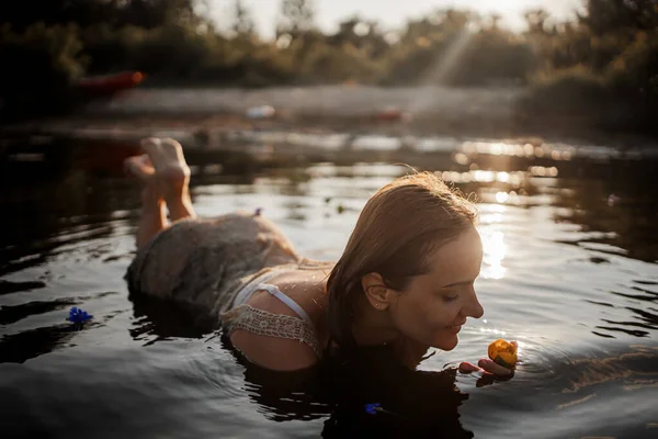 美丽的年轻女子在湖中 夕阳西下 手里拿着百合花 一个浪漫的湿湿的女孩在日落时的画像 温暖的太阳 一个女人的自然美 — 图库照片