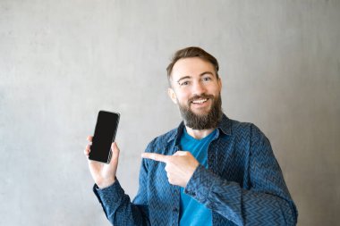 Mobil Uygulama Reklamı. Yakışıklı Heyecanlı Adam Boş Akıllı Telefon Ekran Pozisyonunu Gri Arkaplanda Gösteriyor, Kameraya Gülümsüyor. Şuna bak, cep telefonu görüntüsü.