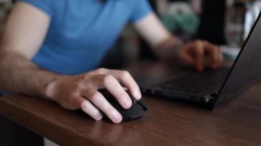 İnsanoğlu fareyi eliyle tutuyor. Adam dizüstü bilgisayarla ahşap masada çalışıyor. Erkek ofis çalışanı sayfaları kaydırıyor..