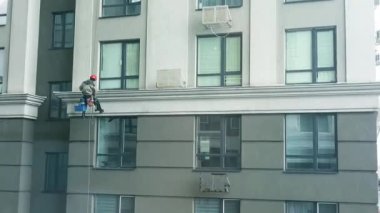 Gökdelen cam temizleyicisi tek başına. Pencere temizleyicileri binanın pervazındaki iplere asılırlar.