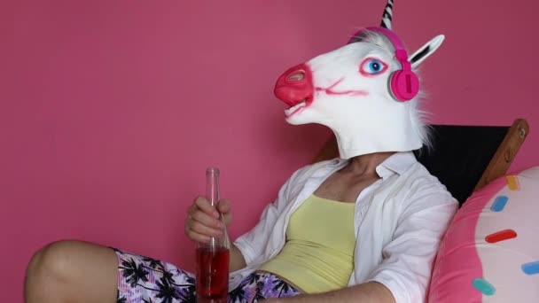 年轻快乐有趣的游客戴着独角兽面具喝啤酒躺在粉红色背景的躺椅上 暑假海上休息日光浴的概念 — 图库视频影像
