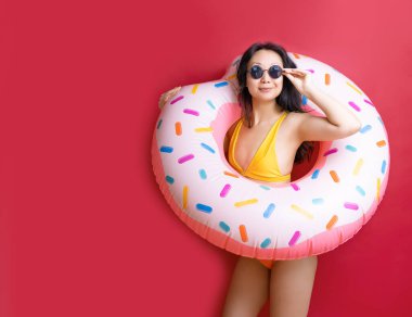 Mutlu eğlenceli genç seksi Asyalı kadın ince mayo giyer pembe şişirilebilir yüzük tutar canlı kırmızı duvar arka planında stüdyo yaz oteli havuzu dinlenme güneşi konsepti