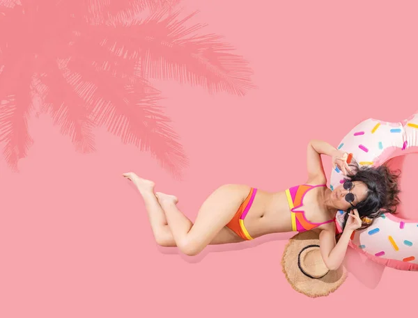 年轻性感的亚洲女人身材苗条 戴着泳衣太阳镜 躺在充气环状酒店游泳池上 隔离在粉红的背景下 暑假海上休息日光浴的概念 — 图库照片