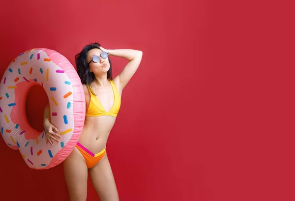 快乐快乐的年轻性感的亚洲女人苗条的身体穿着泳衣抱着粉色的充气环隔离在鲜红的色彩墙的背景工作室夏季酒店游泳池海景日光浴的概念 — 图库照片