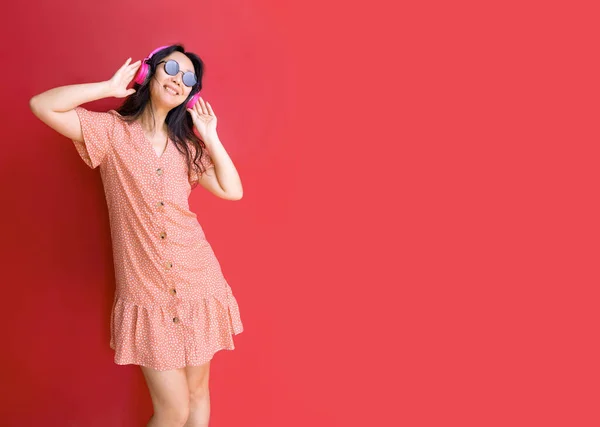 stock image Positive asian woman with headphones dancing in studio against red background.