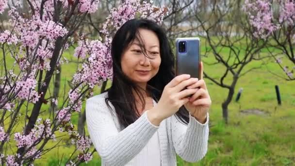 慢动作亚洲女人带着粉红樱花在树上拍照 — 图库视频影像