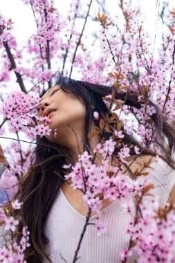 Bahar kızı suratı. Sakura çiçekleri arka planında asyalı bir kadının portresi. Hanami kutlaması Sakura çiçek bahçesinde. Genç bayan Sakura parkında duruyor ve pembenin güzelliğinin tadını çıkarıyor..