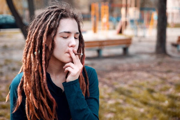 Молодая девушка с дредами курит свернутый джойнтер с бутонами травы внутри крупного плана.
