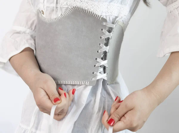 Cropped close-up shot of a lady dressed in a white dress with a wide grey leather belt or corset