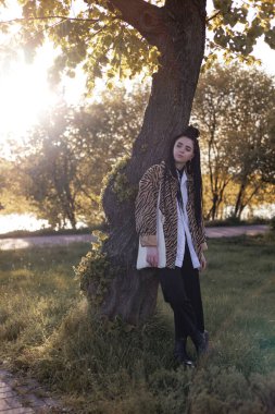 Uzun saçlı, leopar desenli tişörtlü yeşil ormanda dinlenen kadın doğanın sessizliğinin ve güzelliğinin tadını çıkarıyor..