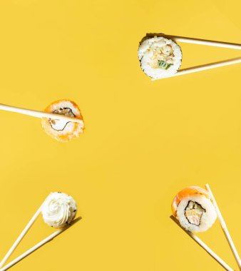 Kadınların elinde sarı arka planda çubuklarla suşi ruloları var. Yaratıcı bir kavram. Kesme yolu.