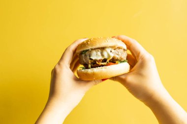 Kadın eli sarı arka planda sıcak lezzetli bir burger..