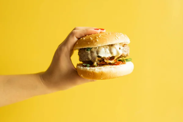 Kadın Eli Sarı Arka Planda Sıcak Lezzetli Bir Burger — Stok fotoğraf