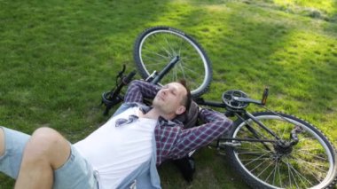 Yaz parkında bisikletin yanında çimlerde yatan genç adam. Bisiklet sürdükten sonra mutlu insan, gözleri kapalı, doğada sessizliğin tadını çıkarıyor. Spor, açık hava aktivitesi, fitness konsepti