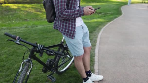 白人サイクリスト男はオフロードバイクパークをスポーツします バックパックを持ったアスリートの男は自然界に座って携帯電話の技術を使って — ストック動画