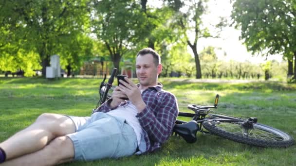 白人サイクリスト男はオフロードバイクパークをスポーツします バックパックを持ったアスリートの男は自然界に座って携帯電話の技術を使って — ストック動画