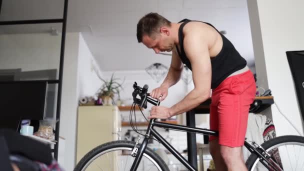 在工作室的公寓里 骑自行车在自行车上安装配件 男人在家里骑自行车 男用自行车在客厅里修理砂砾自行车 你自己解决你的周期 Diy概念 你们自己动手吧 — 图库视频影像
