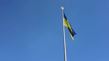 Mavi gökyüzünün altında rüzgarda dalgalanan Ukrayna bayrağı.