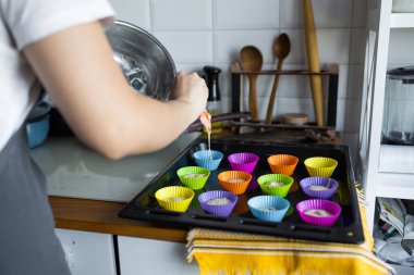 Mutfakta enfes kek yapıyorlar. Dolaplı kek kutusu, malzemeler ve çatal bıçaklar görülüyor. Bir kadın çukurlara karışım ekliyor.