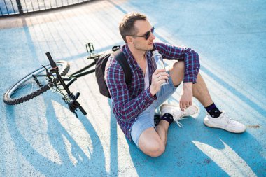 Bisikletli çekici bir adam su içiyor. Aktif sağlıklı yaşam tarzı. Spor adamı doğadaki egzersizden sonra dinleniyor.. 