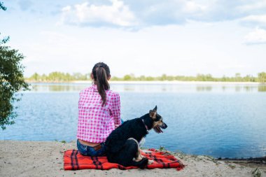Parkta köpekle eğlenen, yaz boyunca battaniyeye oturan bir kadın. Kadın kucaklayan köpek. Evcil hayvanlar ve aşk konsepti.