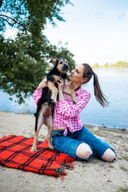 Parkta köpekle eğlenen, yaz boyunca battaniyeye oturan bir kadın. Kadın kucaklayan köpek. Evcil hayvanlar ve aşk konsepti.