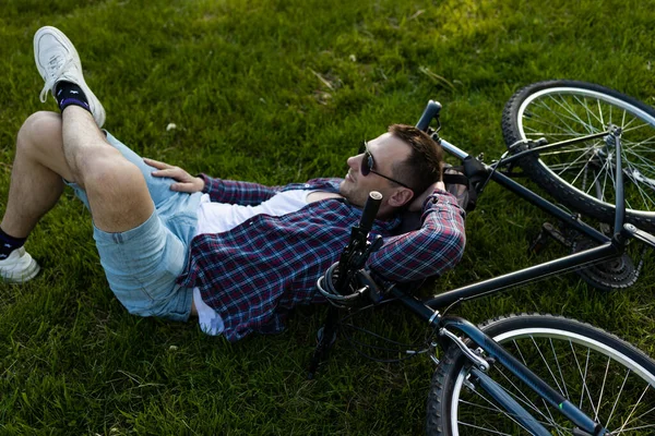stock image Young man resting next to bike in summer park. happy person resting after cycling, eyes closed, enjoying silence in nature. Sport, outdoor activity, fitness concept