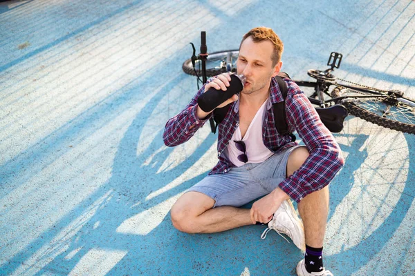 Bisikletli çekici bir adam su içiyor. Aktif sağlıklı yaşam tarzı. Spor adamı doğadaki egzersizden sonra dinleniyor.. 