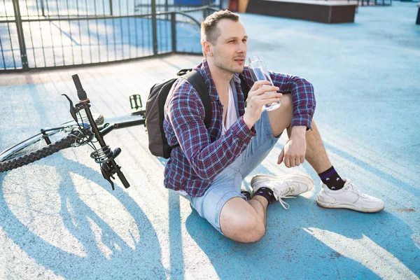 Bisikletli çekici bir adam su içiyor. Aktif sağlıklı yaşam tarzı. Spor adamı doğadaki egzersizden sonra dinleniyor.. 