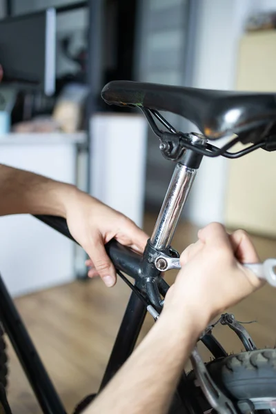Cyclist mounting accessories on bike at home in studio apartment. Man sets up bike at home. Male repairs bicycle in living room gravel bike. Fixing your cycle yourself. DIY concept. Do it yourselves