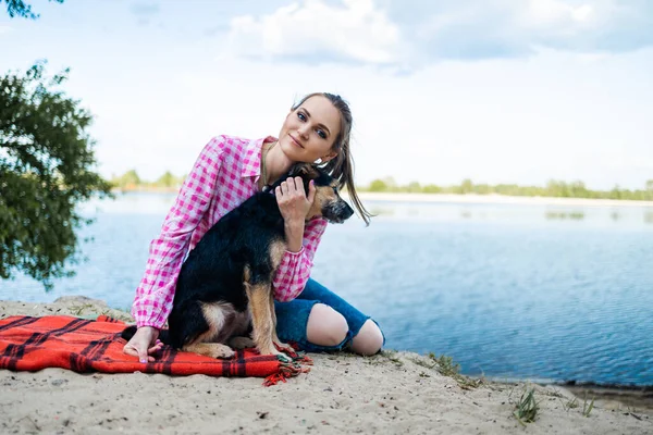 stock image woman having fun with dog in park, sitting on blanket during summer. Woman hugging dog. Pets and love concept.