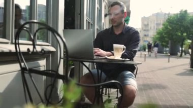 Kafkasyalı iş adamı dizüstü bilgisayarla çalışıyor ve açık şehir kafesinde cep telefonuyla konuşuyor. İş iletişimi ve aygıtlar kavramı.